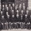 Black and white photo of 40 men in guard uniforms posing for a group photo in front of a building.