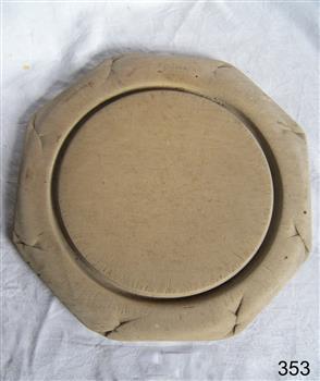 Octagonal wooden breadboard with inner round groove. Has decoration around the outside that is badly worn.