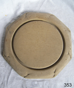 Octagonal wooden breadboard with inner round groove. Has decoration around the outside that is badly worn.