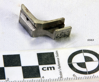 A metal 'L' shaped tool with grooves for fitting to machine and working with the fabric