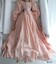 A pink satin doll's dress with gathered sleeves, a frill along the hem, a pink ribbon tied at the waist and a beaded neckline.