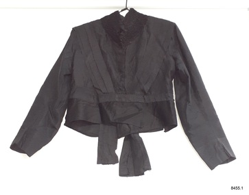 Black silk jacket with long sleeves, stand-up collar and peplum waist.