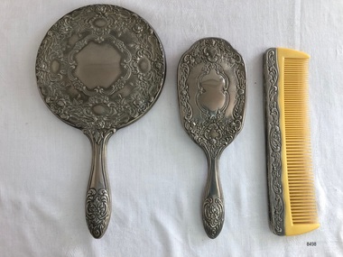 Back view of a three-piece vanity set that includes a hand mirror, hair brush and comb. 