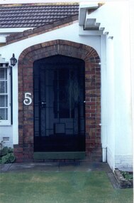 Brown brick arch entrance to porch with cast iron work gate set in rendered house exterior, with lamp light on the left top corner.  House number "5" in white halfway up the arch.