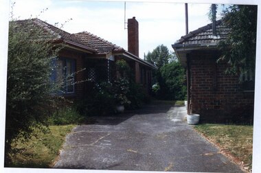 Partial views of the right side of one brown brick house and the left side of a neighbouring brick house which share a drive which narrows to one parking spot at the end.