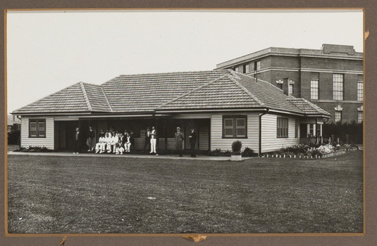 Black and white photograph of a men, some in sporting clothes, posing in front of a sporting club house