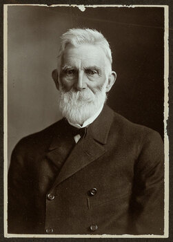 Black and white photograph of a man in a suit with white hair and beard