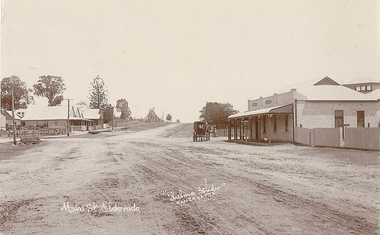 Wide street with buildings on left and right and horse cart on the right.