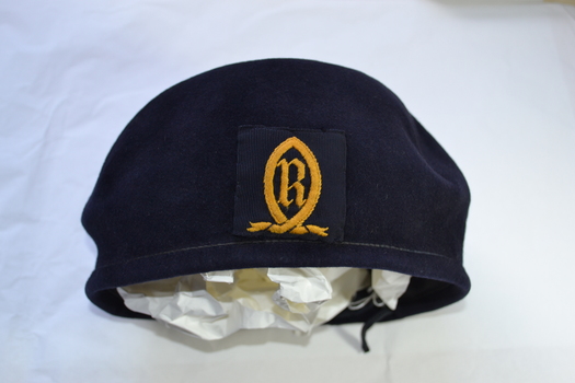 Front view of navy blue wool beret with a school crest embroidered in yellow gold thread attached to the centre front.