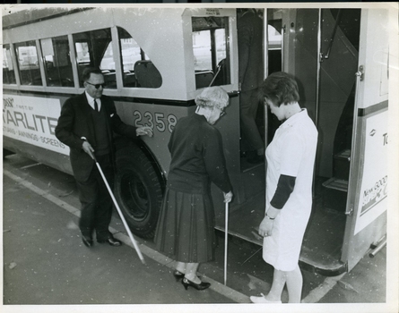 Two people board a bus using their white canes