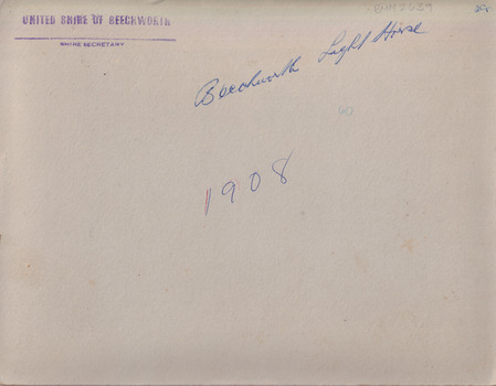 The cream coloured backing of the photo with blue cursive writing and a purple stamp along the top part.