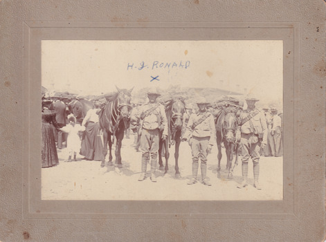 Three soldiers and three horses facing towards camera. Civilians standing in background. Text "H.G Ronald" written on image. Image mounted on card.