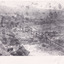 A black and white photograph of a mining landscape and water race with eight individuals standing along the channel. In the background are hills and cottages.