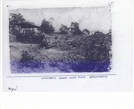 Scattered piles of smashed rock debris. A bearded man in a waistcoat stands near an open-sided timber structure. Three men are seated to the left of standing man.