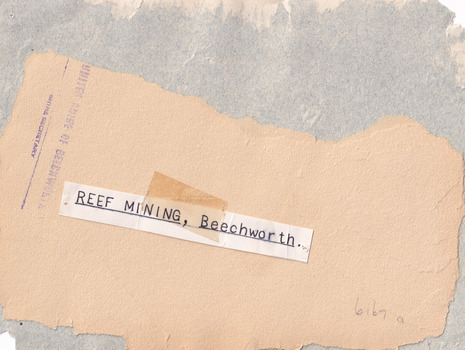 Rear of the aged photograph. Colour is tan, with the top layer of paper peeled off in some places. 