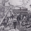 A black and white rectangular photograph depicting 21 separate men, either standing or sitting around a wooden structure.