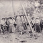 A black and white rectangular photograph depicting men and women standing around mining equipment. 