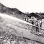 A black and white photograph featuring a group of ten miners standing at a cliff face using a high pressure hose.