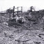 Open mine with bamboo scaffolding leading from left of photo to the centre. A small rectangular boiler/steamer house right behind scaffolding in centre of photo. Men with two horse and carts at top of mine at the right side of the background. 