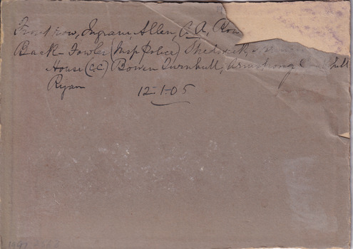 The reverse side of a photograph. The reverse has a large tear in the top right-hand side with text identifying the men in the photo. 