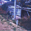 Two unknown men standing in front of a damn and next to an old wooden building that is becoming overrun by foliage. There is farm and perhaps mining equipment of some sort in an annex next to the building. Perhaps an old seam engine that has been converted to a water pump.