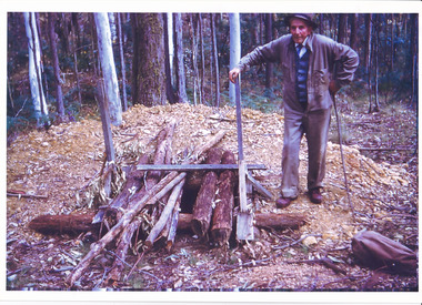 Photograph depicts and unknown elderly gentleman standing next to a mine shaft. Date and location unknown.