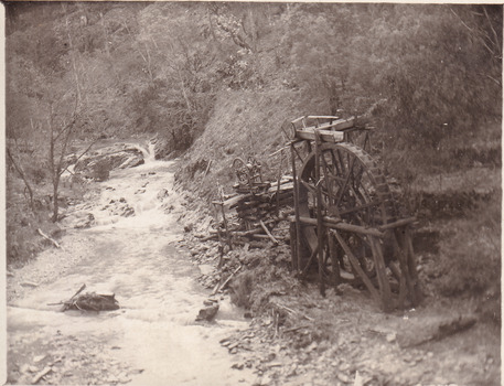 River flowing through scrub towards a metal wheel; part of a mine set up.