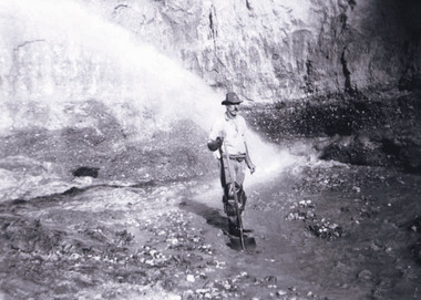 Photograph of a man standing in a wet mining excavation pit holding a shovel