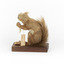 Squirrel standing on a wooden platform clutching an acorn in its hands. Acorns are also located on the platform and a paper tag hands from the specimen's arm.