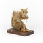 Squirrel standing on a wooden platform clutching an acorn in its hands. Acorns are also located on the platform and a paper tag hands from the specimen's arm.