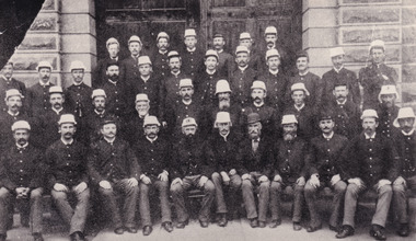 Black and white photo of 40 men in guard uniforms posing for a group photo in front of a building.