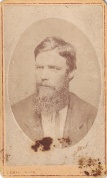 A portrait of light skin tone man, with a long bushy beard, and formally dressed. He is looking off to his right side. 