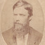 A portrait of light skin tone man, with a long bushy beard, and formally dressed. He is looking off to his right side. 