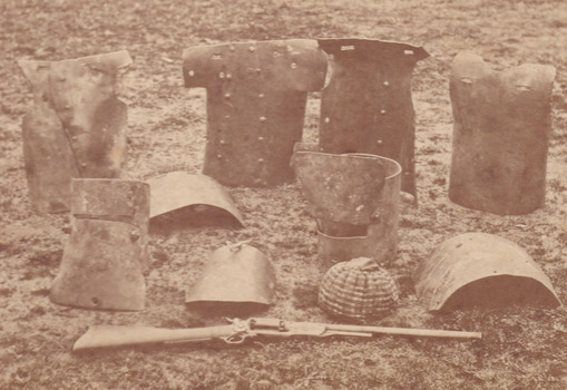 Sepia photograph of Kelly armour including helmets and breastplates arranged on the ground.