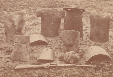 Sepia photograph of Kelly armour including helmets and breastplates arranged on the ground.