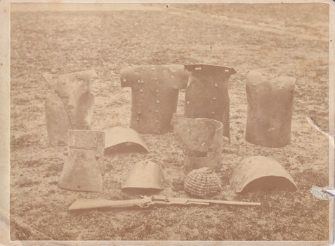 Sepia photograph of the Kelly Gang armour sitting on the ground. A thin border around the main image appears to continue the image in a whiter tone.