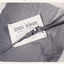 A black and white photograph of a rifle sitting across a poster offering an £8000 reward for robbery and murder. The two objects are resting on a dark material which sits on a shaggy surface. The image has a thin white border.