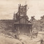 An image taken of Cock's Pioneer  G & T Sluicing No. 4 site looking east. The image depicts several people, including a Mr Hollister (left), Mrs Breustedt (4th from left), the children Min and Chris Breustedt, and Kate Timmons holding a girl's hand, standing underneath the verandah of the timber and tin-roof structure.