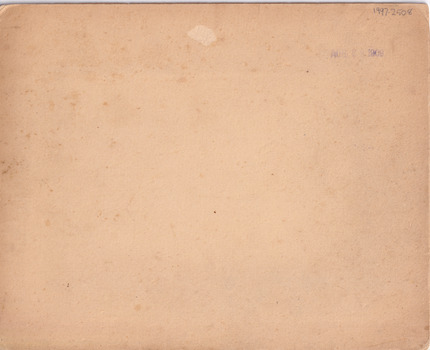 Rear of an aged photograph. Colour is tan with dark and light spots visible and fraying around the edges.