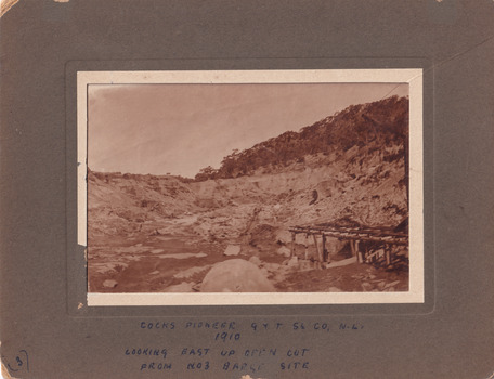 Image with wide frame taken at El Dorado Cocks Pioneer Gold and Tin Sluicing Company looking east up open cut from barge site. Image depicts unevenly cut rock with a small timber structure on the right of the image