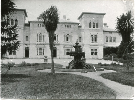 View of Mayday Hills hospital. Large building with lawn in front with fountain and some trees.