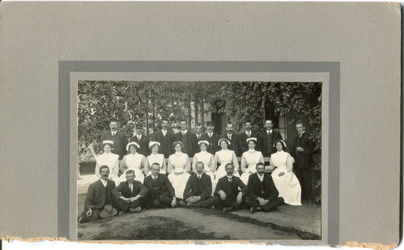 Mounted photograph of mental hospital staff, nurses and male workers. 16 men in 2 rows, with a row of female nurses in between. 2 men in the photo have 'Kepi' style hats.