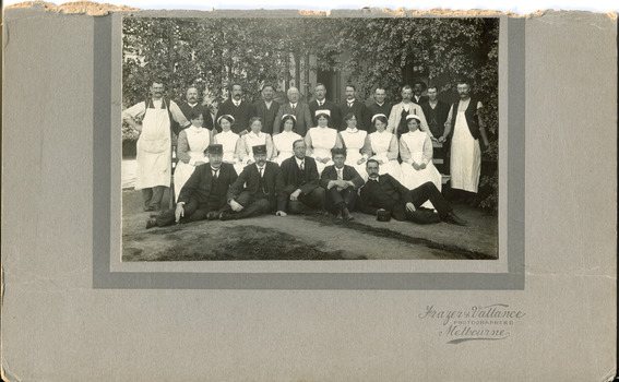 Photograph of mental hospital staff, nurses and male workers. 17 men in 2 rows, with a row of female nurses in between. 2 men in the photo have 'Kepi' style hats.