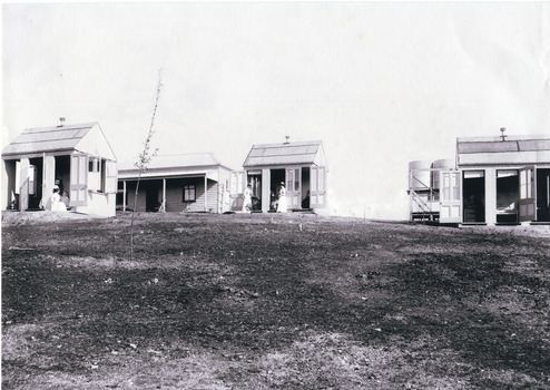 Black and white copy of a photograph depicting weatherboard dwellings, nurses and water tanks