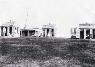 Black and white copy of a photograph depicting weatherboard dwellings, nurses and water tanks