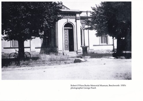 Black and white photograph of the Burke Museum. There are two trees in the foreground which both have bicycles leaning on them.