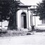 A cropped black and white photograph of the Burke Museum. There are two trees in the foreground which both have bicycles leaning on them.