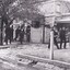 Black and white image of a cobblestone street with a group of men walking in black suits and bowler hats