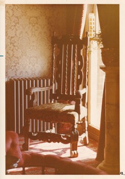 A photograph of a corner of a room featuring a vintage high-back arm chair next to a window.