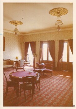A photograph of a vintage  room with two poker tables, a lounge and french windows along one wall.